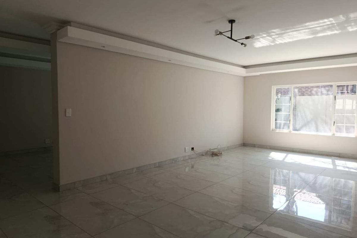 A bright, spacious living area featuring polished porcelain floor tiles, recessed ceiling detailing, and large windows allowing for ample natural light.