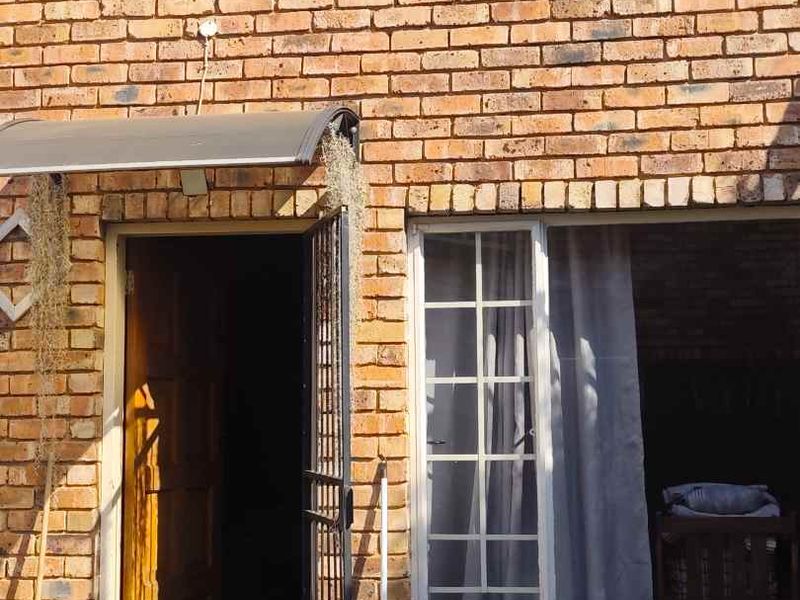 Front entrance of a face brick townhouse featuring a security gate, protective awning, and window bars.