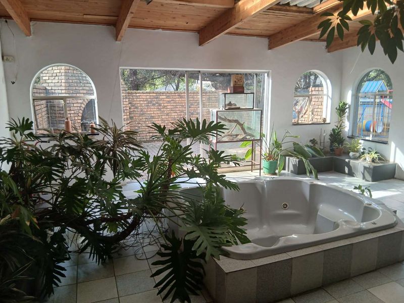 Enclosed patio area featuring a built-in jacuzzi, exposed timber ceiling beams, tiled flooring, and large arched windows overlooking the garden.