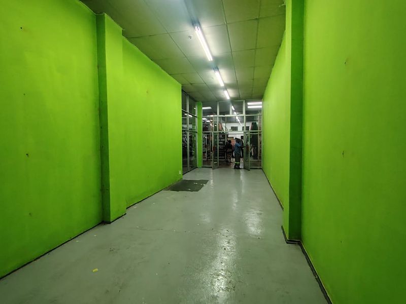 A commercial hallway or corridor featuring bright green painted walls, concrete flooring, and a glass storefront entrance leading to a retail space.
