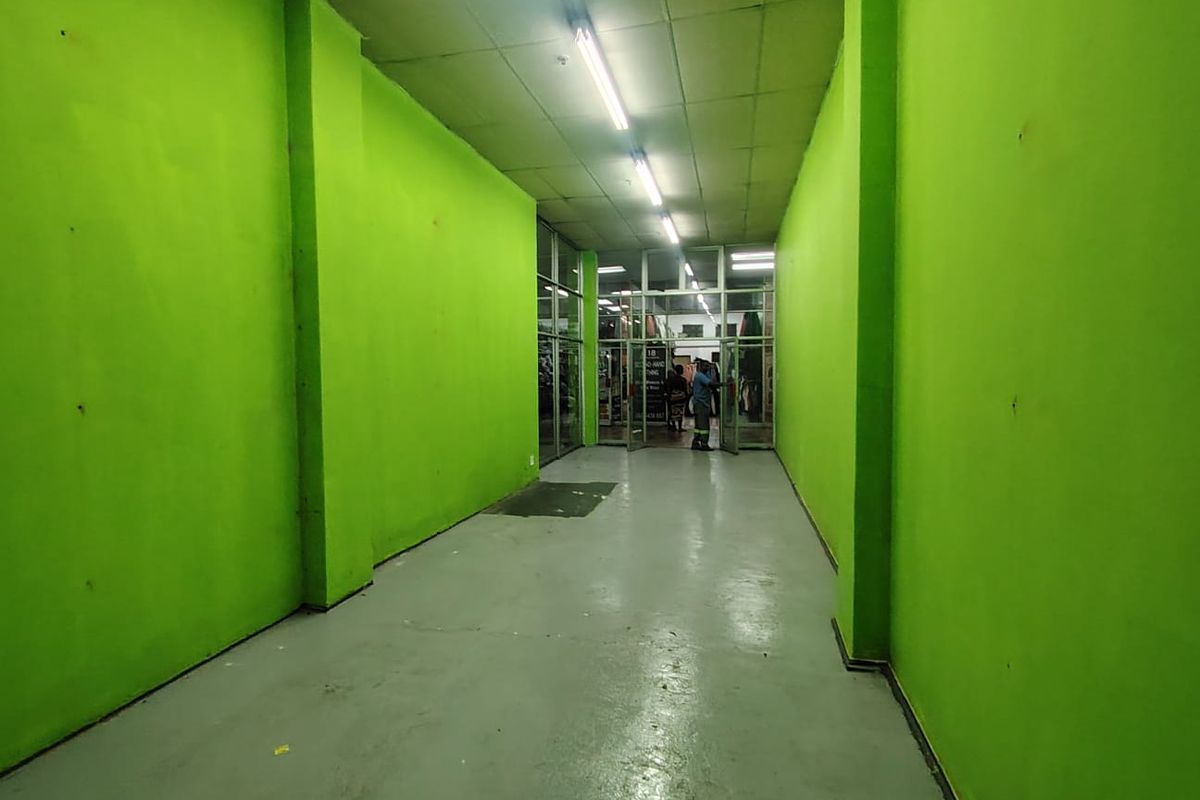 A commercial hallway or corridor featuring bright green painted walls, concrete flooring, and a glass storefront entrance leading to a retail space.