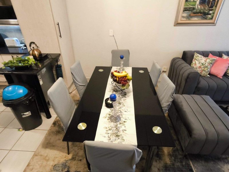 An open-plan living and dining area featuring tiled flooring and a compact kitchen with built-in cabinetry and integrated appliances.