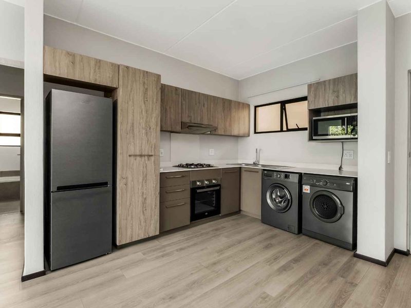 Modern kitchen featuring wood-look cabinetry, gas hob, built-in oven, extractor fan, and integrated laundry appliances with light laminate flooring.