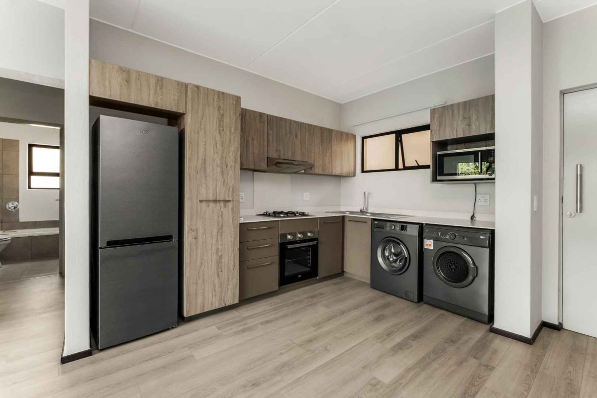 Modern kitchen featuring wood-look cabinetry, gas hob, built-in oven, extractor fan, and integrated laundry appliances with light laminate flooring.