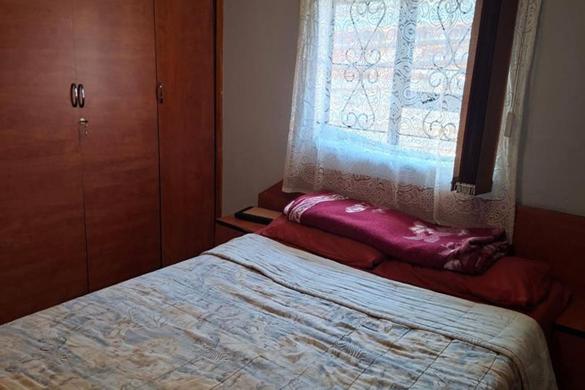 A bedroom featuring built-in wooden cupboards and a window with security bars, providing functional storage and natural light.