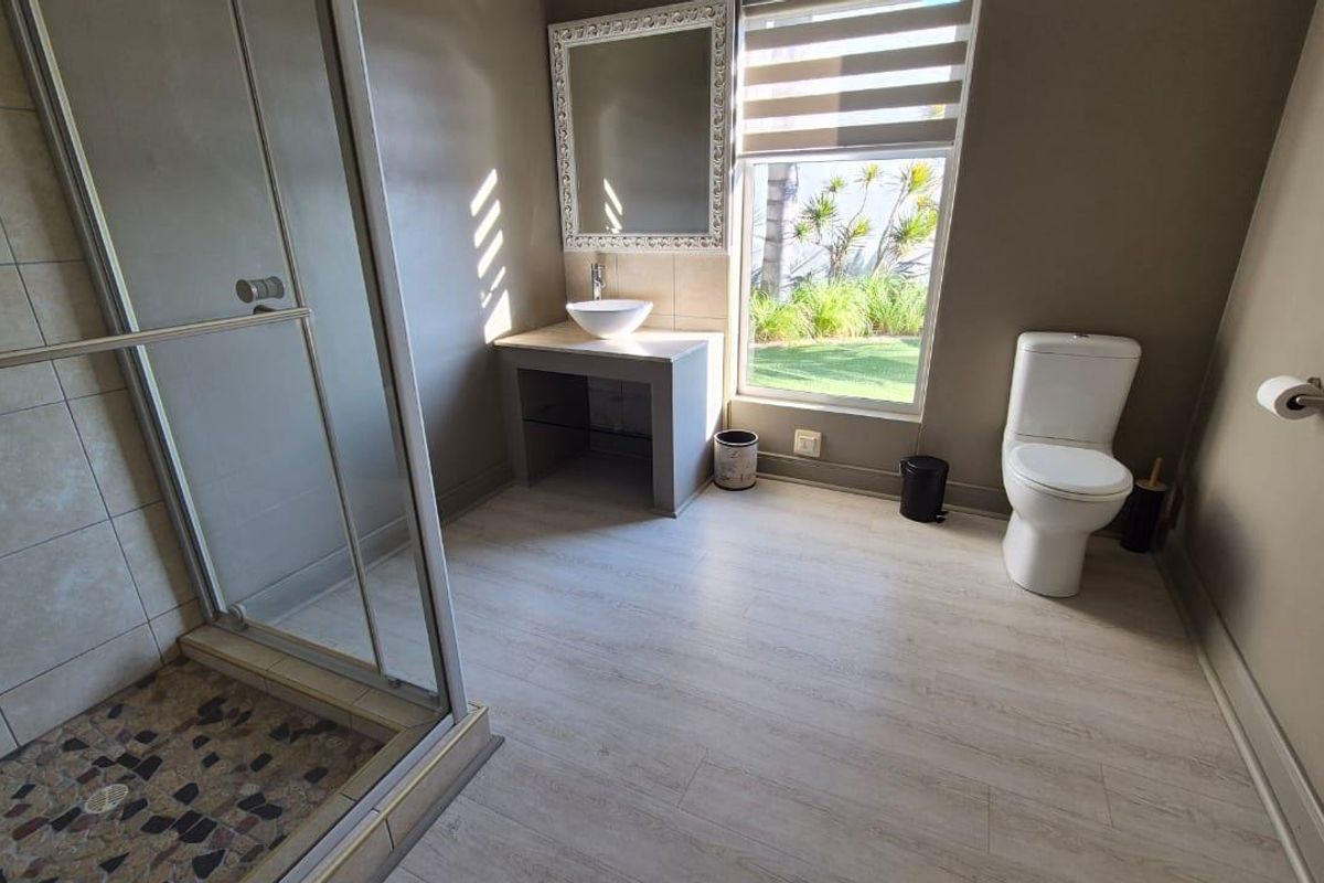 Modern bathroom featuring a glass-enclosed shower with pebble flooring, a vessel sink vanity, and a large window providing natural light.