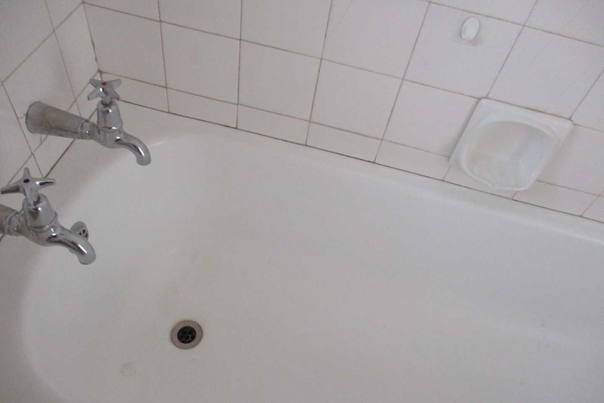 A dated bathroom featuring a standard white bathtub with chrome faucets and white ceramic wall tiling.