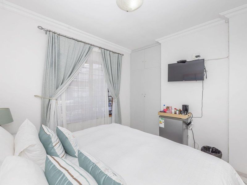A functional bedroom featuring a built-in wardrobe, neutral finishes, and a window with curtain rod, providing a clean and simple living space.