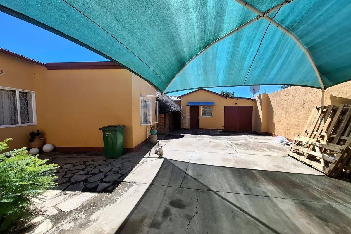 Rear courtyard area featuring concrete and stone paving, enclosed by boundary walls and covered by a large shade sail structure.