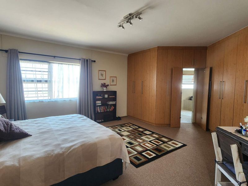 Spacious bedroom featuring extensive built-in wooden cabinetry, neutral carpeting, and a large window with security bars, offering ample storage and natural light.