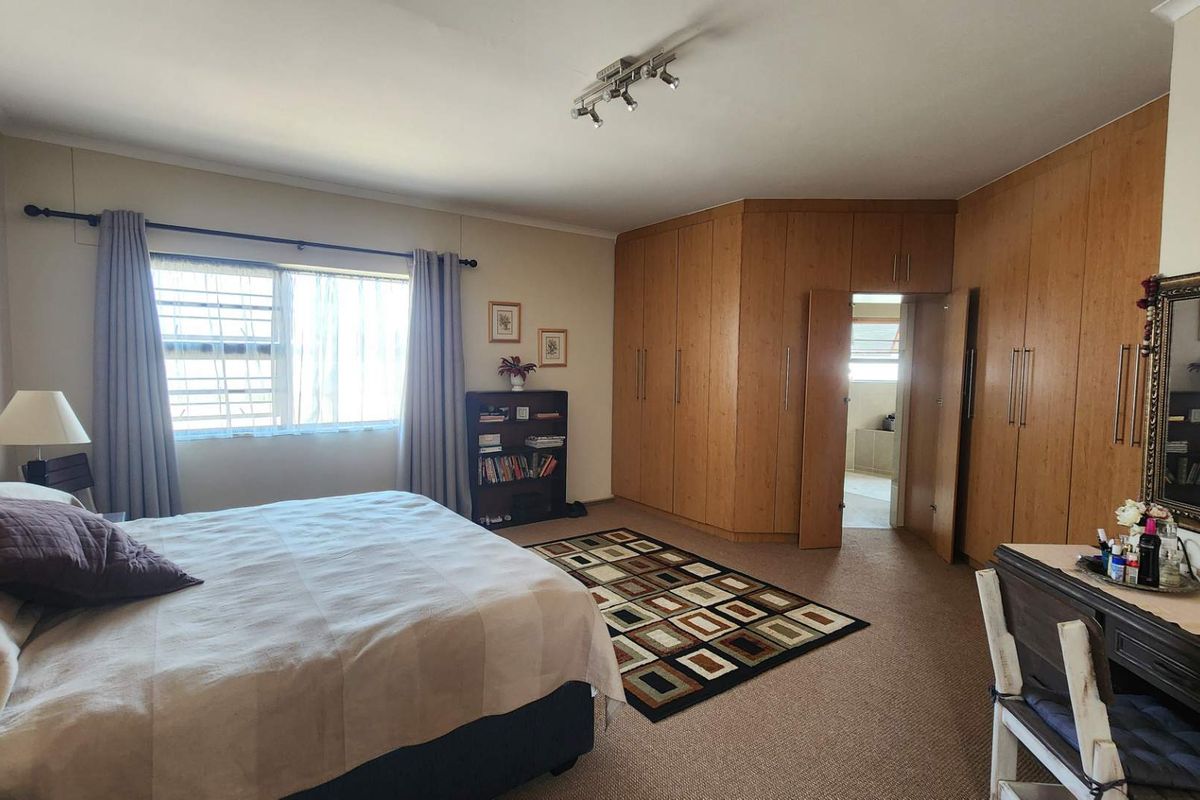 Spacious bedroom featuring extensive built-in wooden cabinetry, neutral carpeting, and a large window with security bars, offering ample storage and natural light.