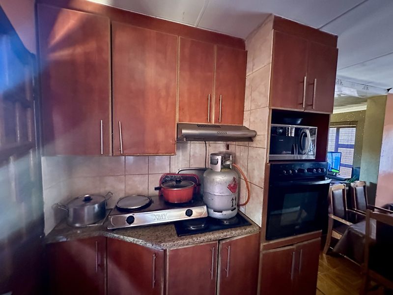 A compact kitchen featuring wooden cabinetry, a built-in oven, extractor fan, and tiled backsplash with granite countertops.
