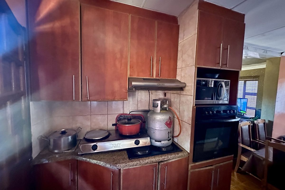 A compact kitchen featuring wooden cabinetry, a built-in oven, extractor fan, and tiled backsplash with granite countertops.