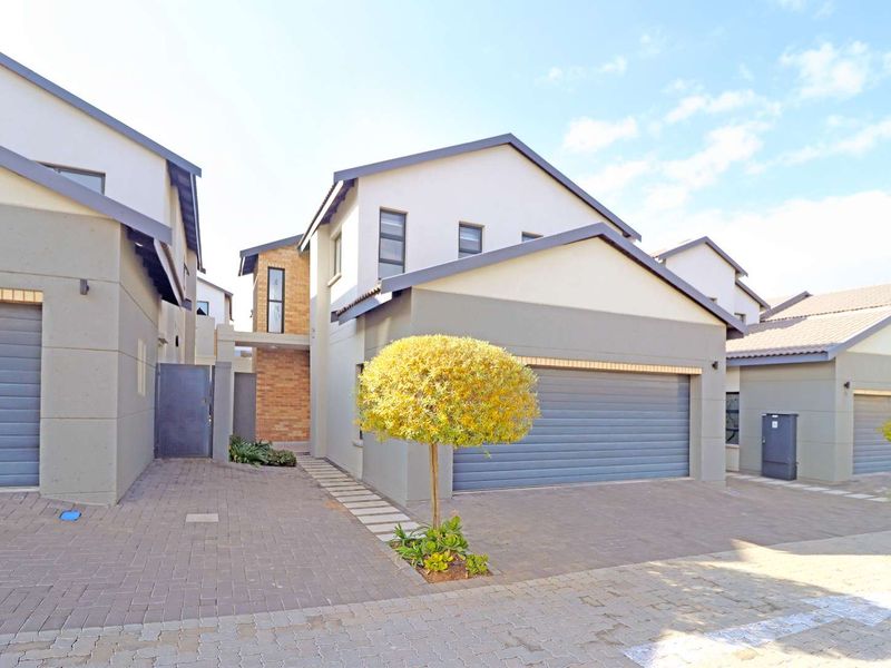 Modern townhouse exterior featuring a double garage, paved driveway, and contemporary architectural design with a combination of brick and rendered finishes.