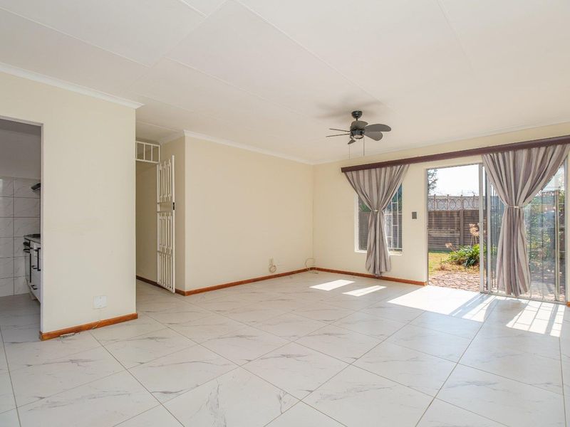 Spacious open-plan living area featuring modern tiled flooring, a ceiling fan, and direct access to the rear garden through a sliding glass door.