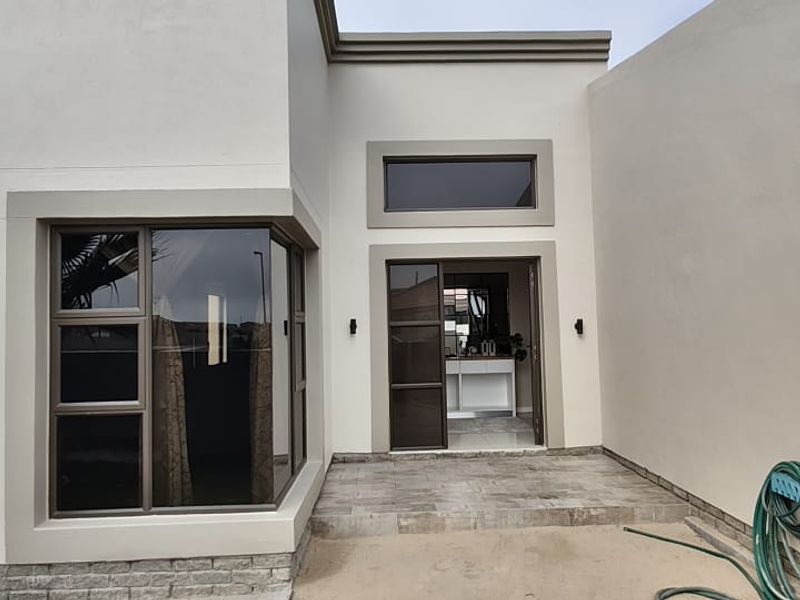 Modern front entrance featuring a tiled porch, aluminium window frames, and contemporary exterior lighting on a clean plastered facade.