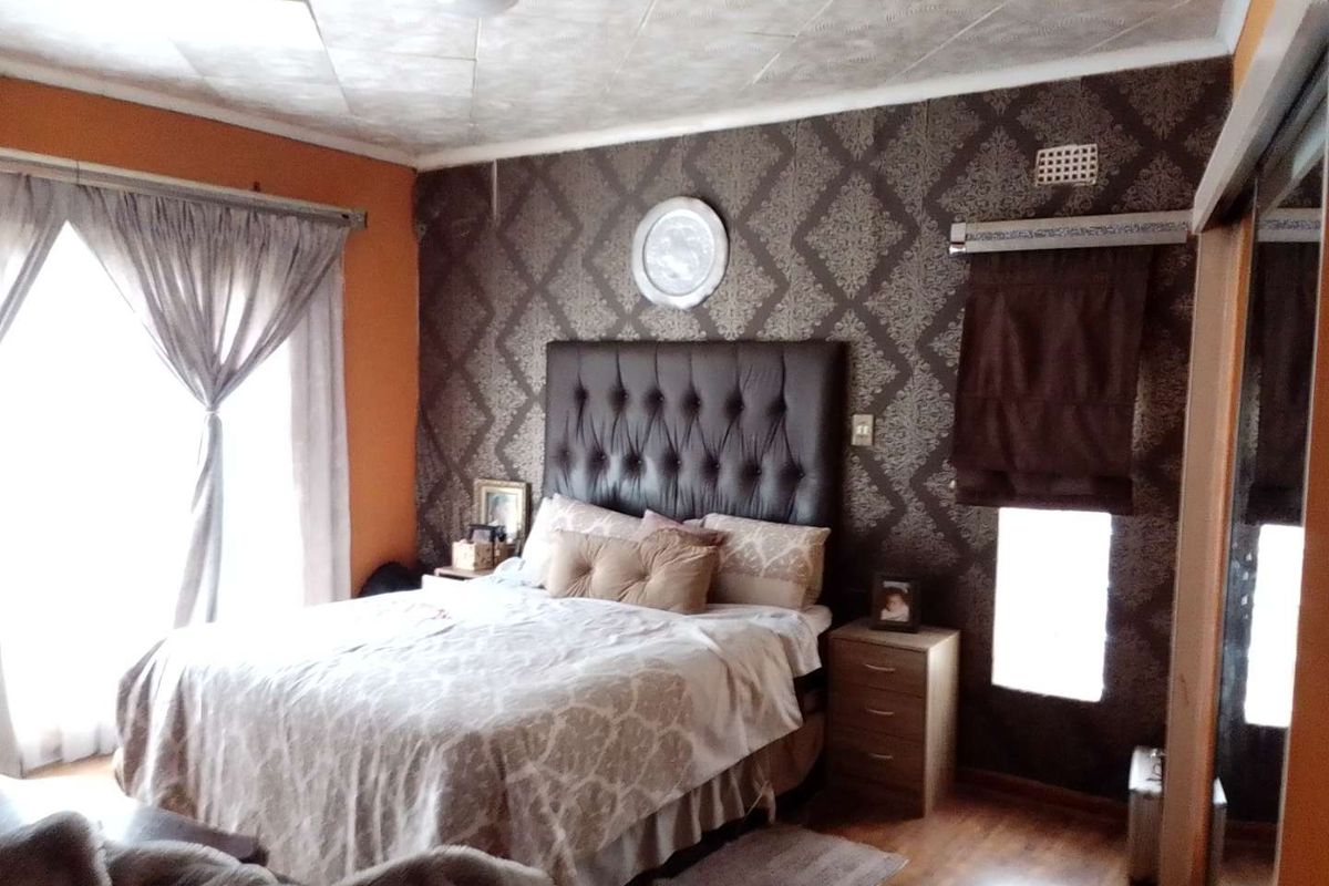 A bedroom featuring patterned wallpaper, a tufted headboard, and laminate flooring, offering a functional space with potential for modern updates.