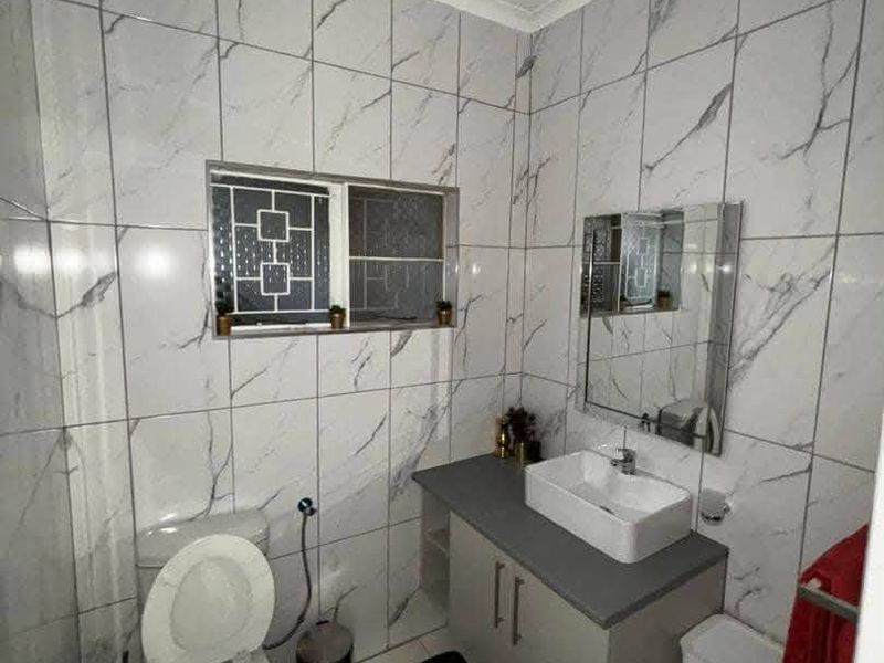 A modern bathroom featuring marble-look wall tiles, a vanity cabinet with a countertop basin, and a wall-mounted mirror.