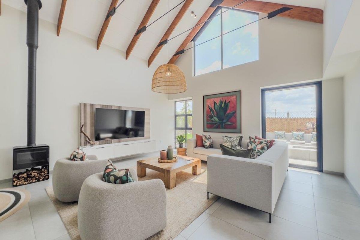 Spacious living room featuring a high vaulted ceiling with exposed timber beams, a modern wood-burning fireplace, and large windows providing abundant natural light.