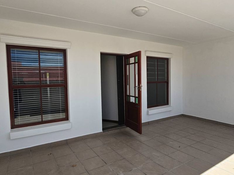 A clean, covered patio area featuring tiled flooring and timber-framed windows, providing a versatile outdoor space for relaxation or entertainment.