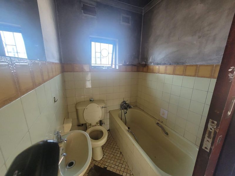 A dated bathroom featuring a bathtub, toilet, and pedestal basin, requiring significant renovation and cosmetic updates to the walls and flooring.