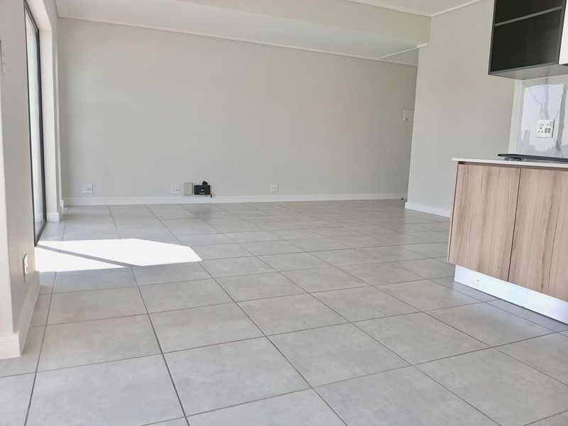 A bright, empty open-plan living area featuring neutral tiled flooring and direct access to an outdoor space through a large sliding glass door.