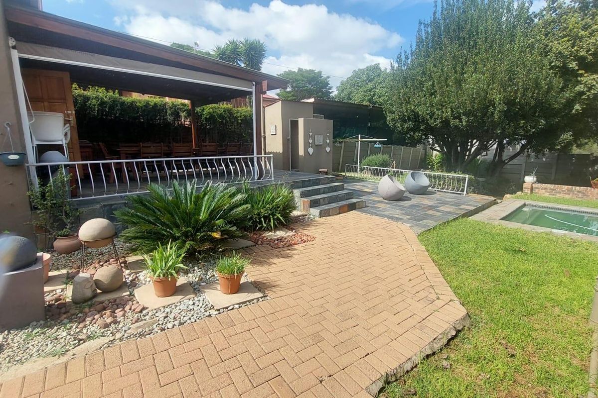 A spacious outdoor entertainment area featuring a covered patio, paved terrace, swimming pool, and landscaped garden.