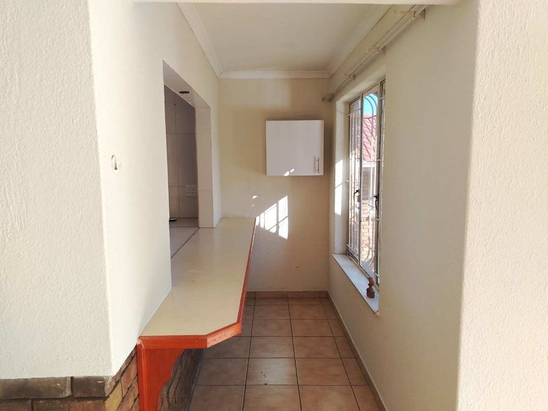 A functional scullery or utility area featuring tiled flooring, a built-in breakfast bar, and a window with security bars.