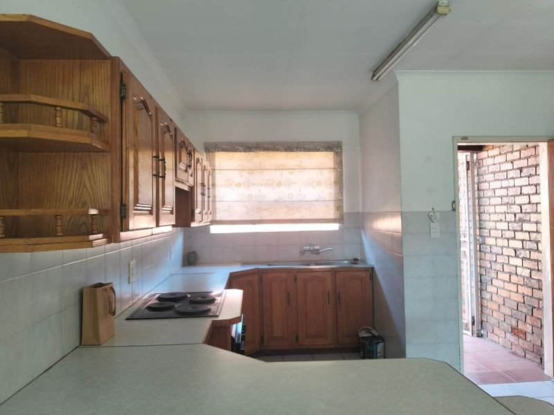 A functional kitchen featuring traditional wooden cabinetry, laminate countertops, an integrated electric hob, and a tiled splashback, offering potential for modern renovation.