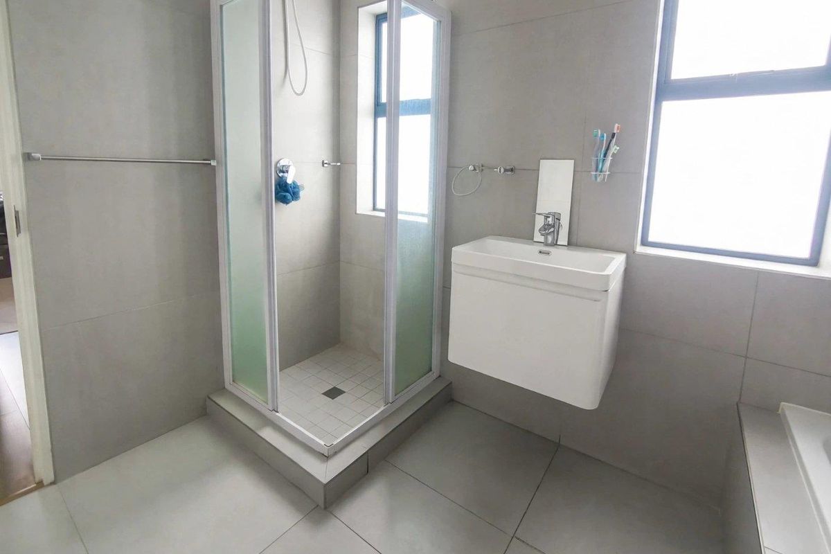 Modern bathroom featuring a glass shower enclosure, wall-mounted vanity with basin, and neutral grey floor-to-ceiling tiling.