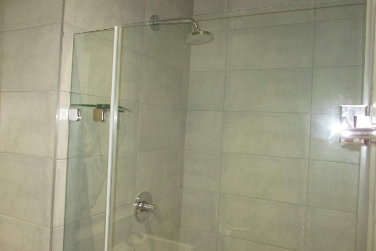 A modern walk-in shower featuring large format grey wall tiles, a glass shower screen, and a chrome rainfall shower head.