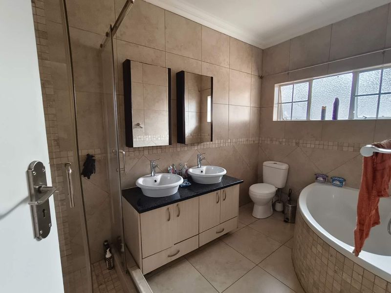 A well-appointed bathroom featuring a double vanity with vessel sinks, a glass-enclosed shower, a bathtub, and neutral tiled finishes throughout.