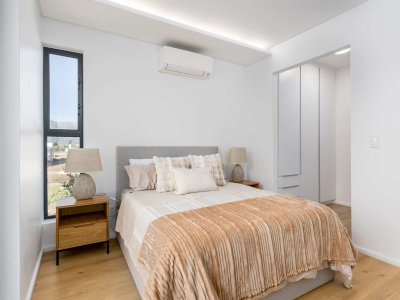 A modern, well-lit bedroom featuring laminate flooring, built-in cupboards, and a wall-mounted split-system air conditioner.
