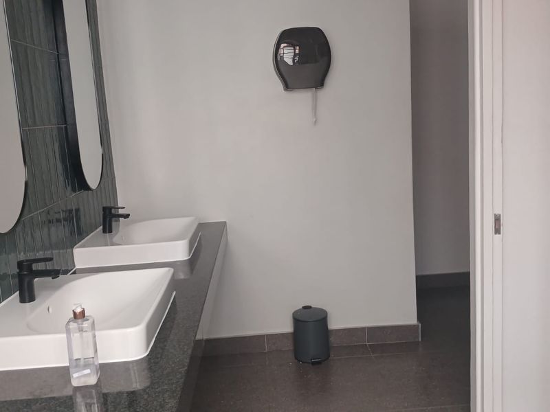A clean, modern industrial-style bathroom featuring a double vanity with vessel sinks, dark tiled splashback, and neutral floor tiles.