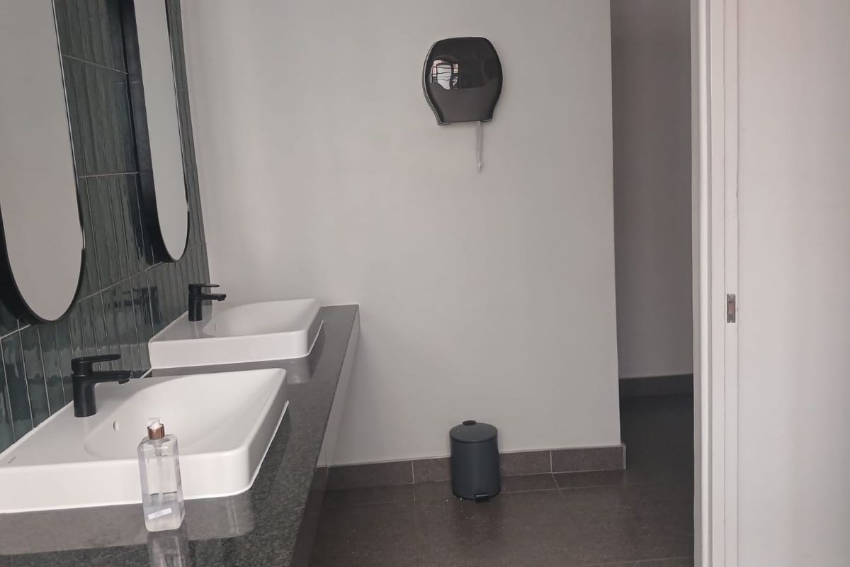 A clean, modern industrial-style bathroom featuring a double vanity with vessel sinks, dark tiled splashback, and neutral floor tiles.
