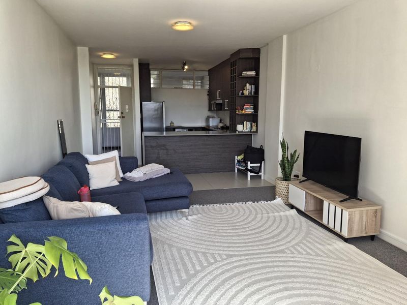 Open-plan living area featuring a kitchen with breakfast bar, built-in cabinetry, and shelving, seamlessly flowing into a carpeted lounge space.