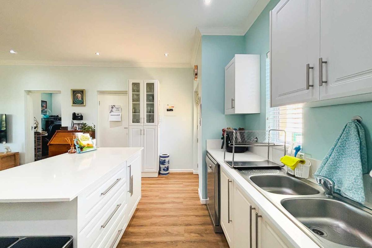 Modern kitchen featuring a central island, double basin sink, ample built-in cabinetry, integrated dishwasher, and light-toned laminate flooring.