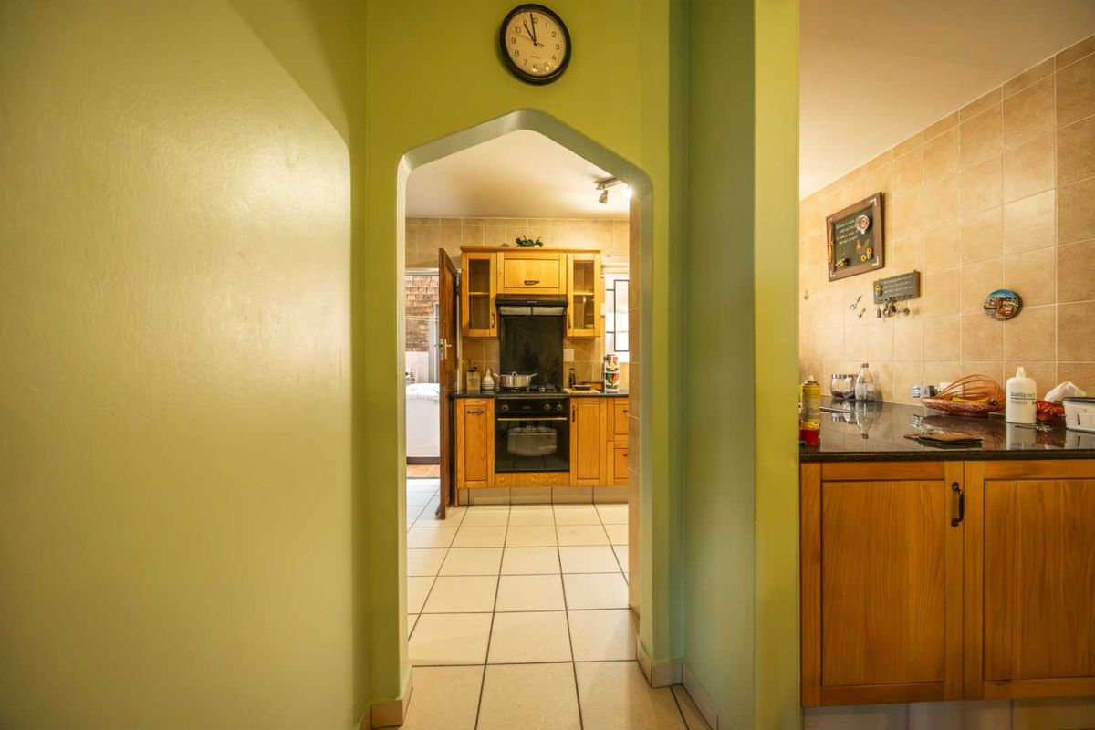 A view through an archway into a kitchen featuring wooden cabinetry, granite countertops, built-in oven, hob, and tiled finishes.