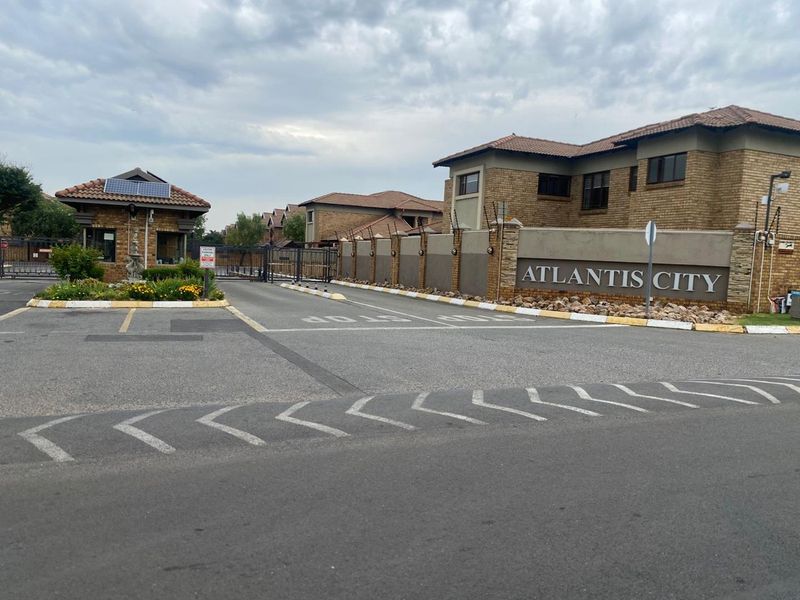 The entrance to Atlantis City complex featuring a secure guard house, perimeter wall with electric fencing, and a paved driveway.