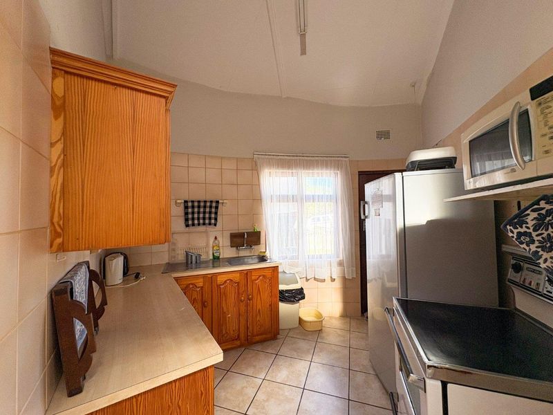 A functional kitchen featuring wooden cabinetry, tiled backsplash, and tiled flooring, offering a dated aesthetic with potential for modernization.