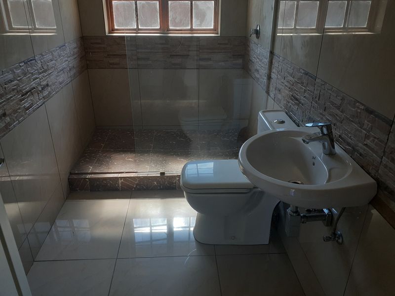 A modern bathroom featuring a walk-in shower with a glass screen, a wall-mounted basin, and a toilet, finished with neutral wall and floor tiles.