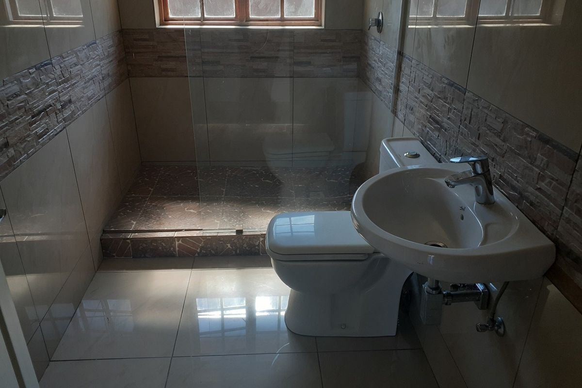 A modern bathroom featuring a walk-in shower with a glass screen, a wall-mounted basin, and a toilet, finished with neutral wall and floor tiles.