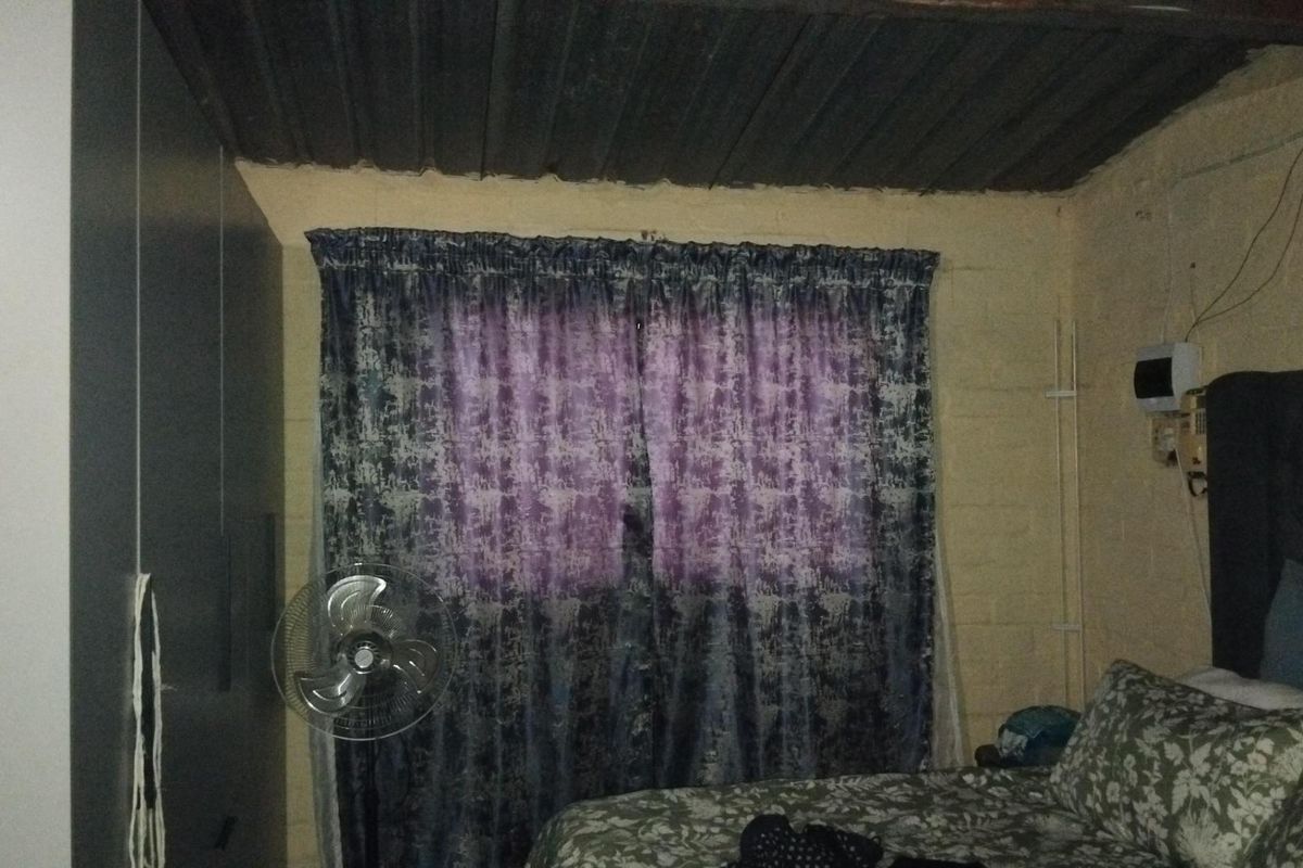 A bedroom featuring exposed corrugated metal ceiling, unfinished masonry walls, and basic window treatments.