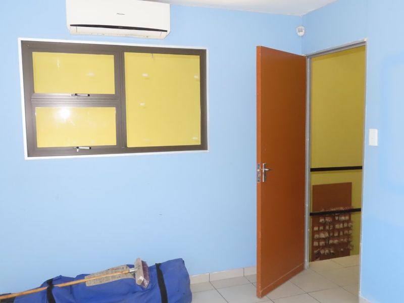 A vacant office space featuring tiled flooring, a wall-mounted air conditioning unit, and an aluminium window frame.