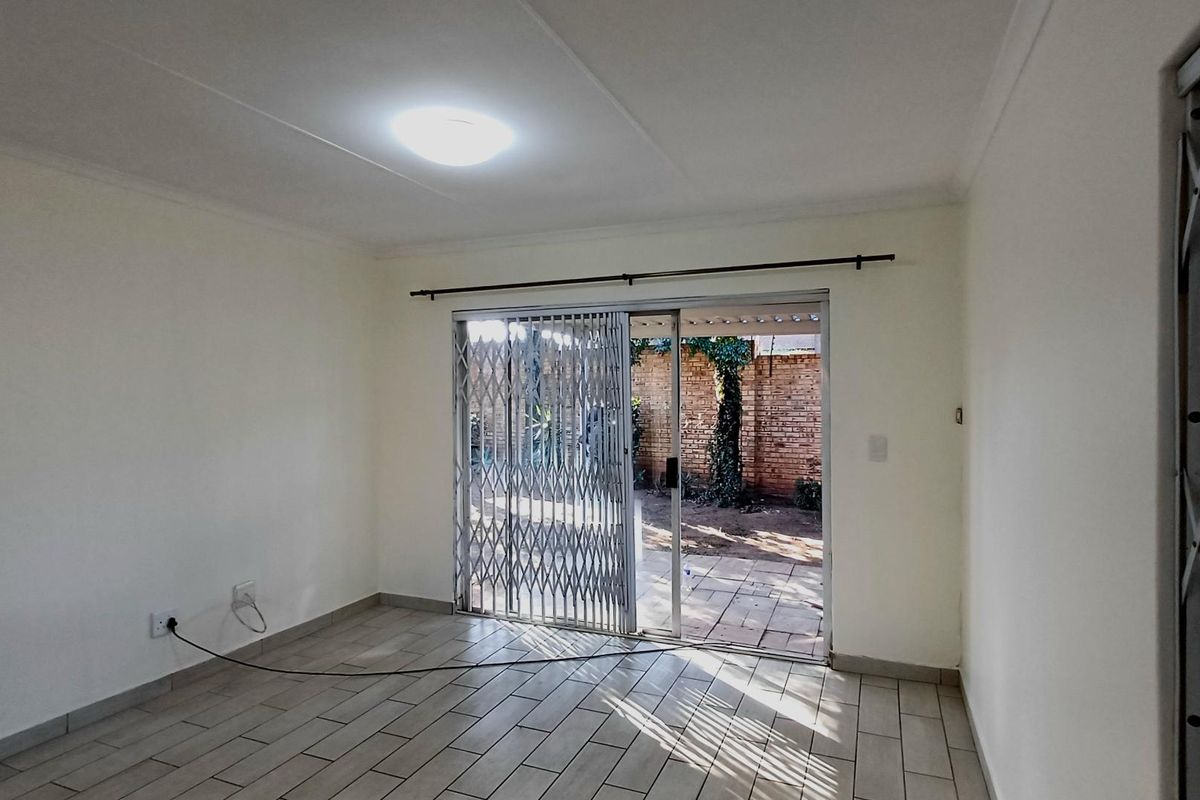 An empty living room featuring tiled flooring, a ceiling light, and a sliding glass door with a security gate leading to an outdoor patio area.