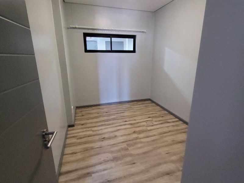 A clean, empty bedroom featuring modern light-toned laminate flooring, neutral walls, and a functional sliding window.