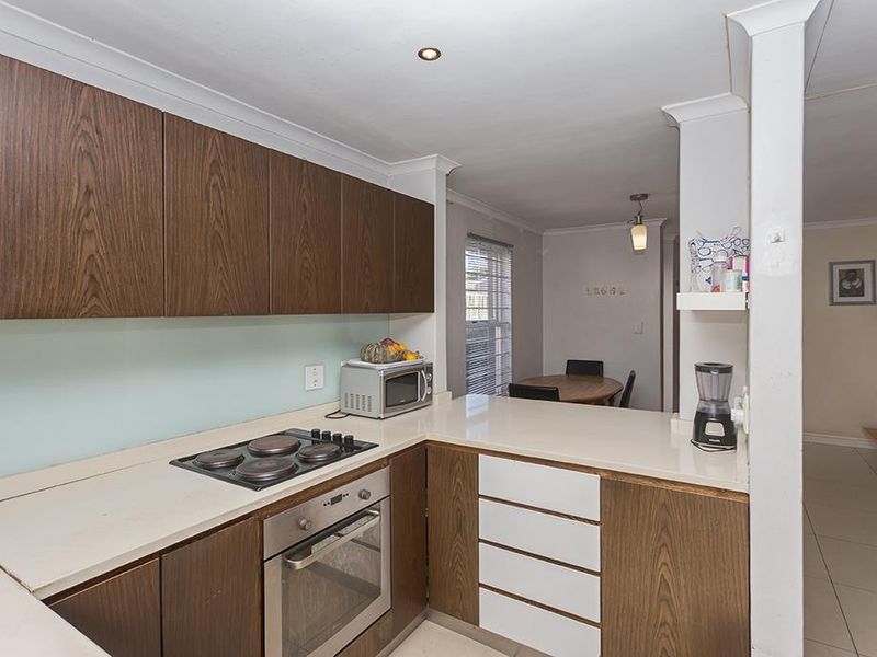 A functional kitchen featuring dark wood cabinetry, stone countertops, a built-in electric hob, and an oven, with an open-plan layout leading to the dining area.