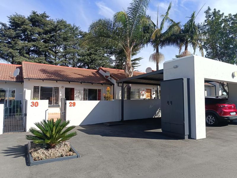 Front exterior view of a townhouse complex featuring a paved driveway, covered carport, and secure entrance with security gates and bars.