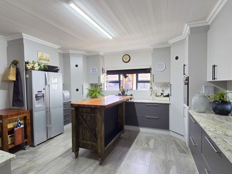 Modern kitchen featuring two-tone cabinetry, stone countertops, a central wooden island, and a tongue and groove ceiling with integrated lighting.