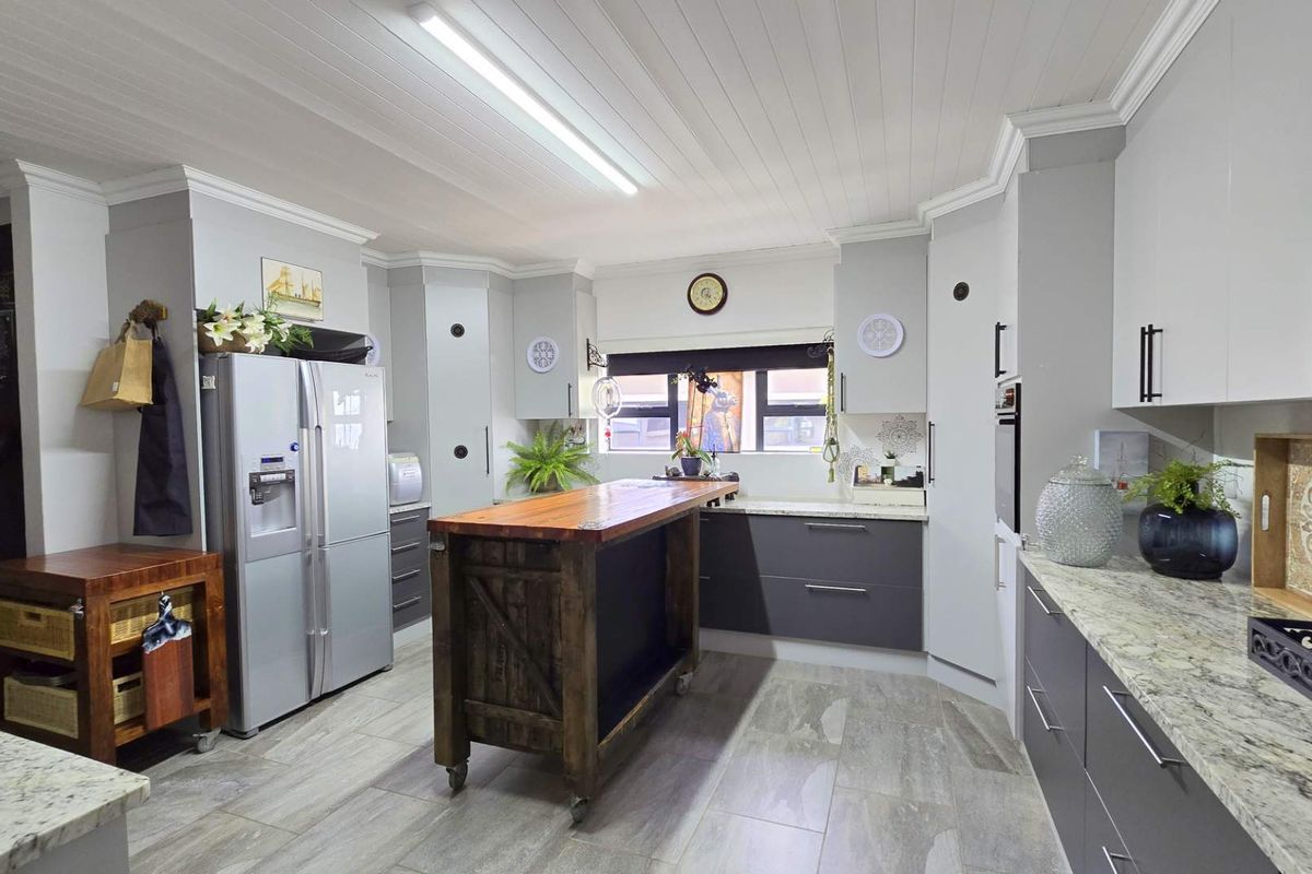 Modern kitchen featuring two-tone cabinetry, stone countertops, a central wooden island, and a tongue and groove ceiling with integrated lighting.